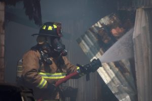 A fireman sprays a hose with a walkie on his shoulder that requires a distributed antenna system